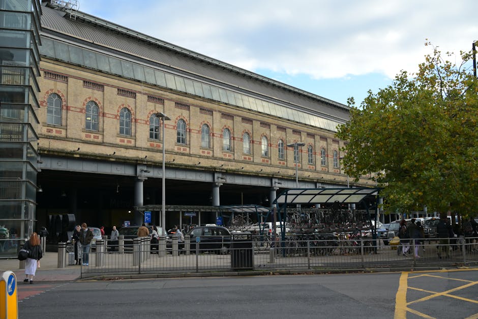 Image of the exterior entrance to Hanwell Station, displaying brickwork with two black and white signs reading 'HANWELL STATION' mounted on either side of a doorway. Above the entrance, a blue sign wi